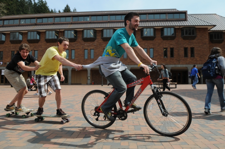 Freshman Tyler Will, left, holds on for a ride on a skateboard from sophomore Will Moore, center, and Jackson Owens on a bike Wednesday, May 3 in Red Square. Photo by Daniel Berman/The A.S. Review